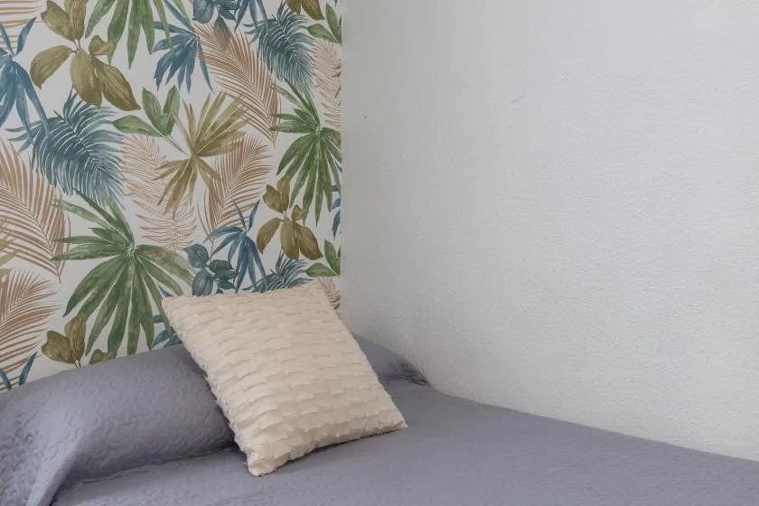A bed with a textured pillow sits beside a tropical leaf-patterned wall.