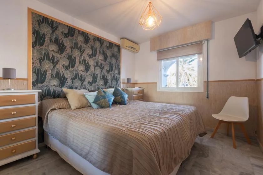A bedroom with a large bed, patterned wall covering, and a window.