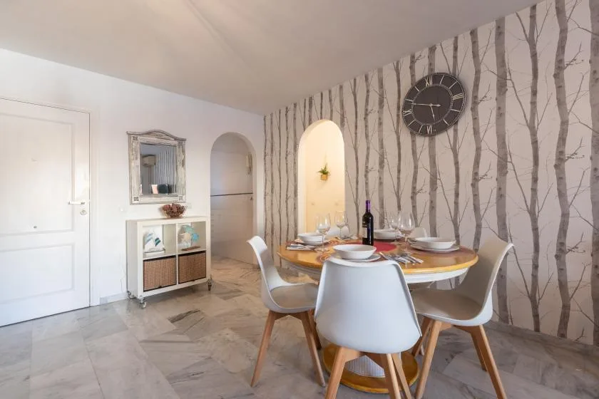 A dining area with a round table and chairs beside a tree-patterned wall.