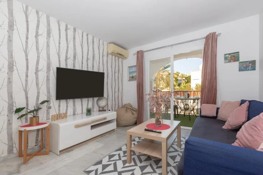 A living room with a television, seating, and glass doors opening to a balcony.