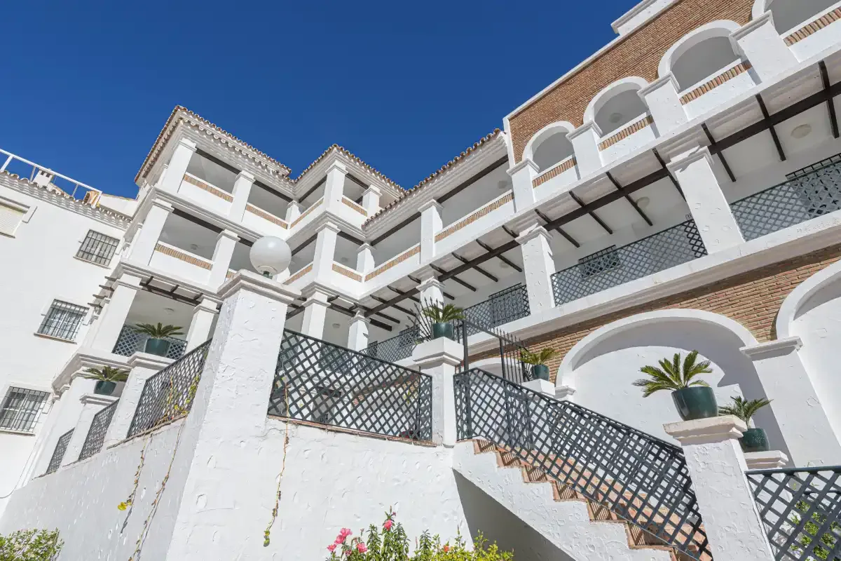 A white multi-story building with balconies and exterior stairs beneath a clear blue sky.