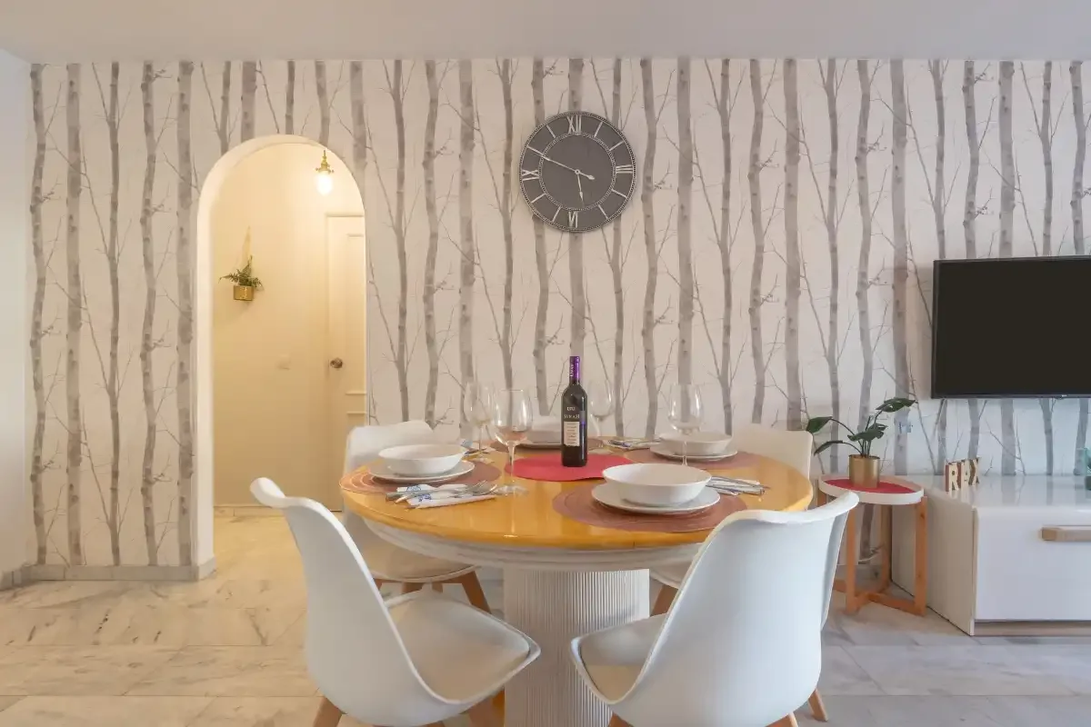 Dining area with a round table and white seating beside a patterned wall.