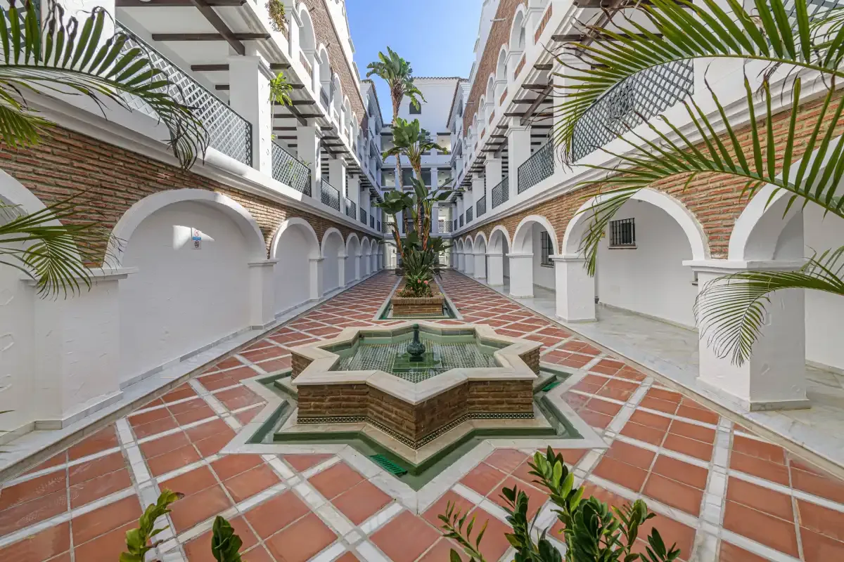 A tiled courtyard with a central fountain is surrounded by white arcades.