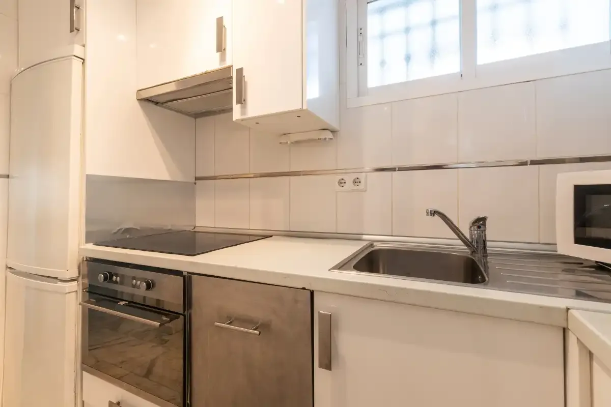 A compact kitchen with a stovetop, sink, and white cabinets.