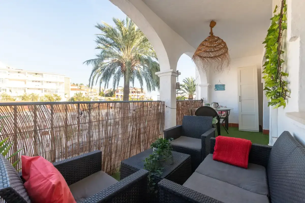 A covered balcony seating area overlooks palm trees and nearby buildings.