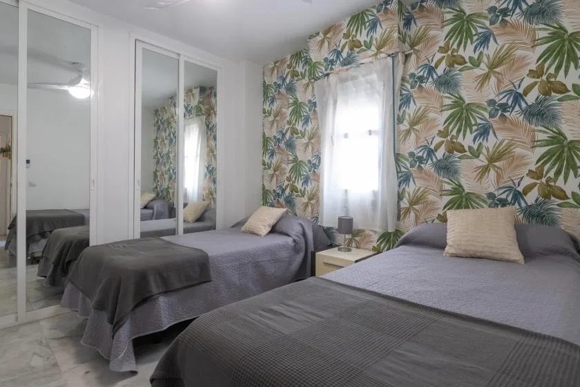 A bedroom with two beds, mirrored wardrobes, and tropical leaf-patterned wallpaper.