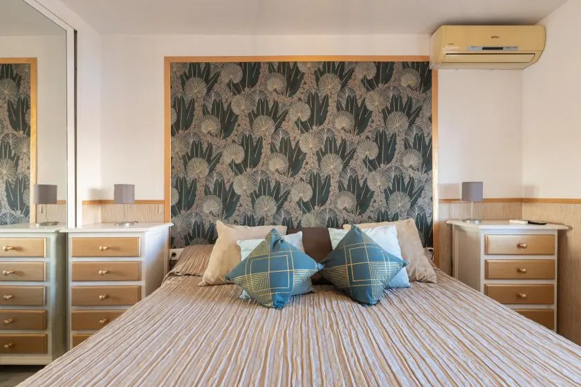 A bedroom with a bed, patterned wall panel, and matching bedside cabinets.