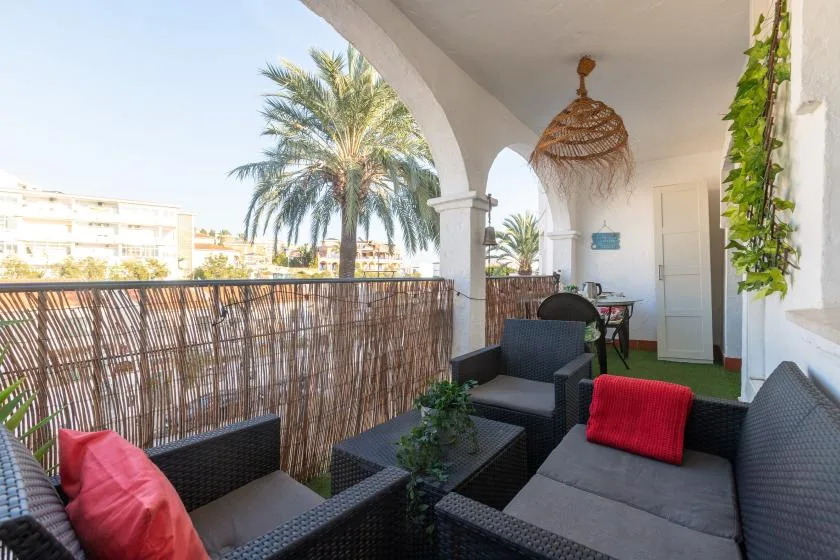 A covered balcony seating area overlooks palm trees and nearby buildings.