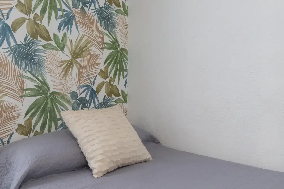 A cushioned seating area beside a wall with leafy botanical wallpaper.