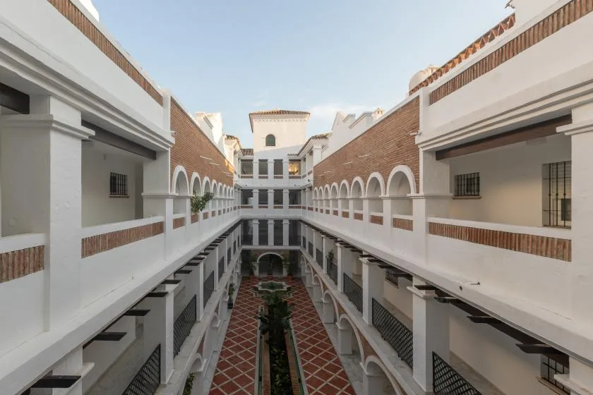 A courtyard between white buildings has arched walkways and a tiled path.