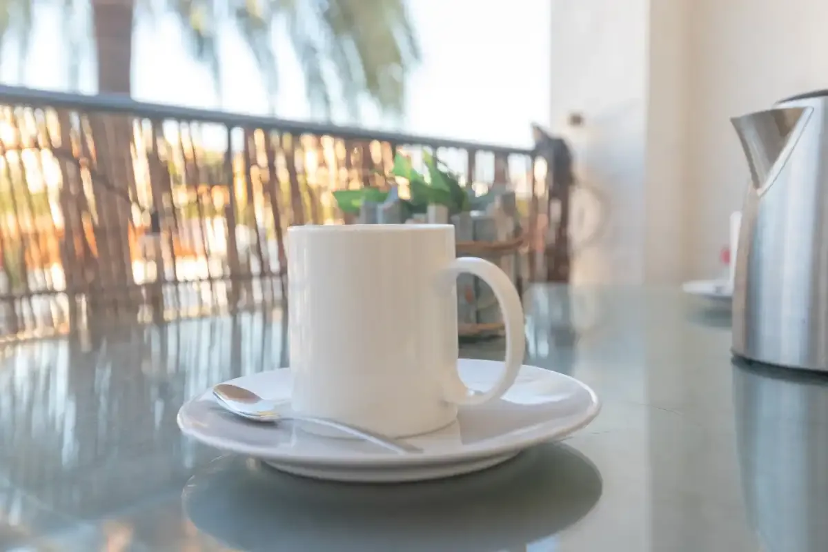 A cup and saucer sit on a table beside an electric kettle.