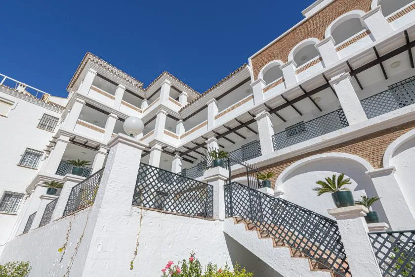 A white multi-story building with balconies and an exterior staircase under a clear blue sky.