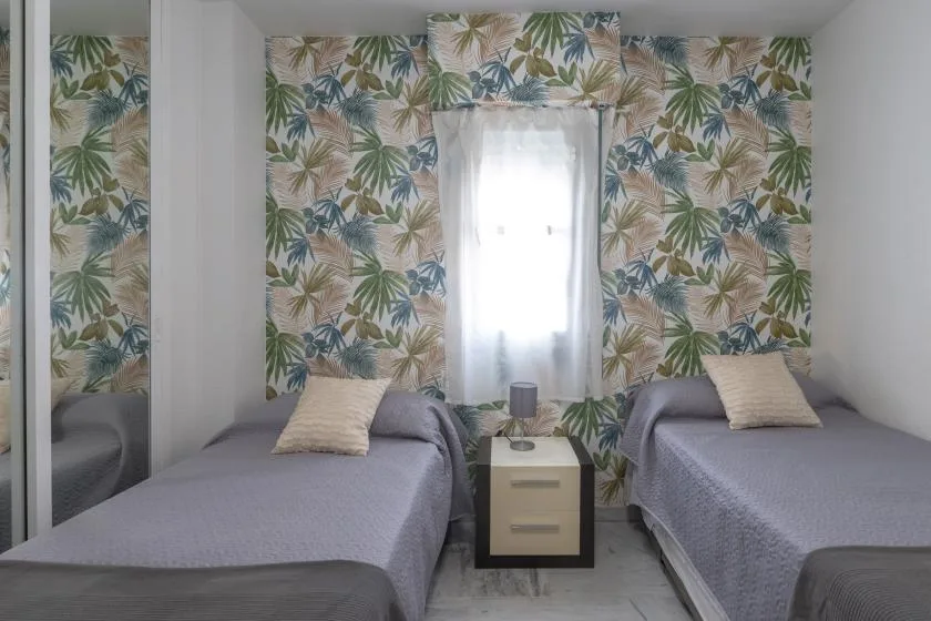 A bedroom with two single beds beneath leafy patterned wallpaper.