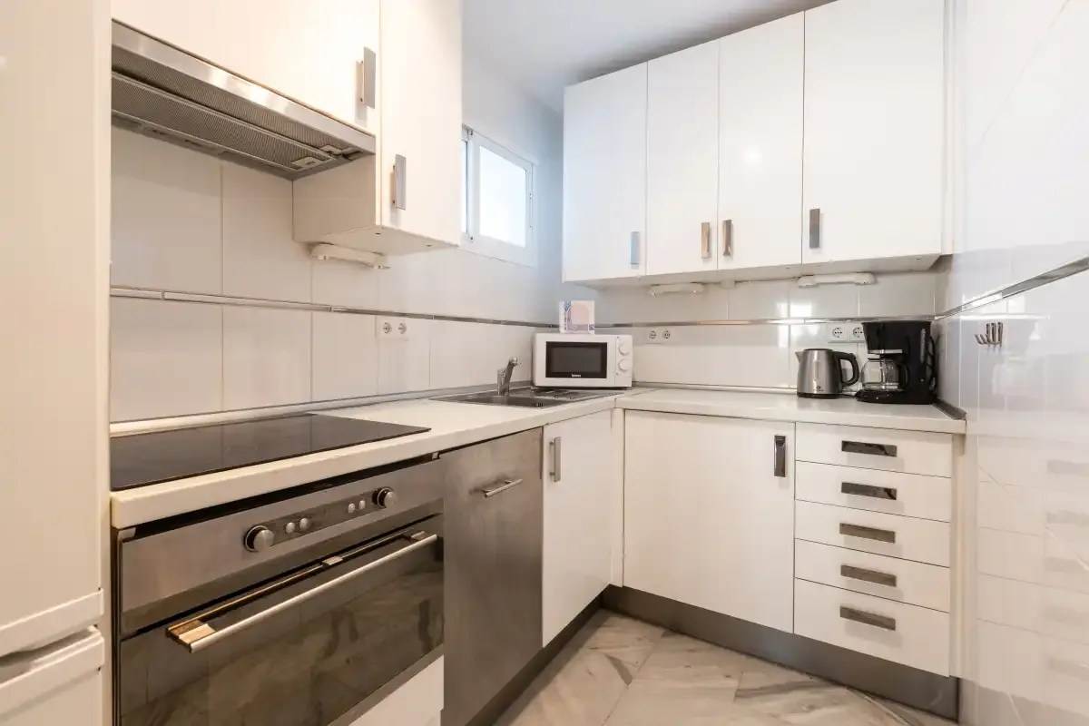 A bright kitchen with white cabinets, a cooktop, and countertop appliances.