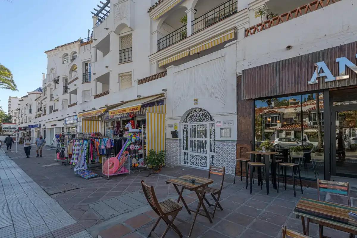 A pedestrian street lined with white buildings, shops, and outdoor café seating.