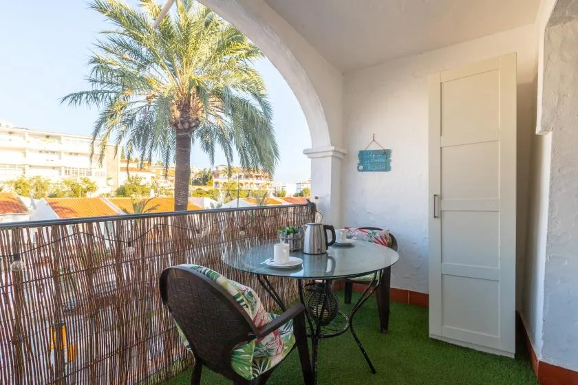 A small balcony with a round table and seating overlooks palm trees.