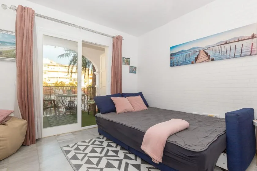 A bedroom with a dark bed, pink curtains, and glass doors opening onto a balcony.