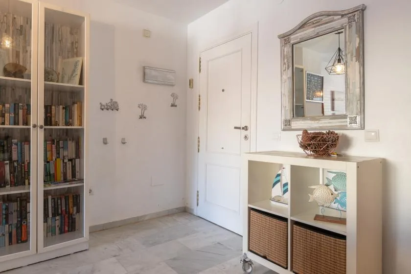 A bright entryway with a white door, bookcase, and storage console.