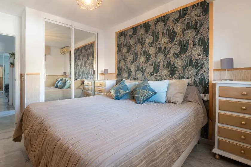 A bedroom with a large bed, blue pillows, and a leafy patterned wall.