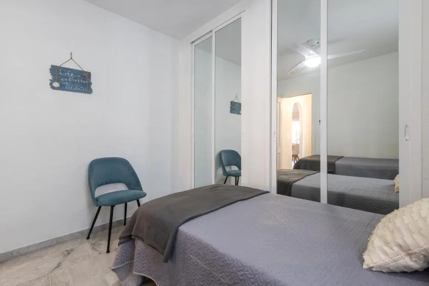 A bedroom with a bed, a chair, and mirrored closet doors.