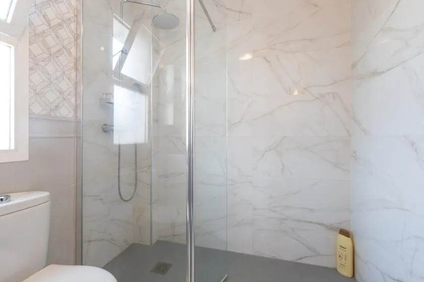 A bright bathroom with a glass shower and pale tiled walls.