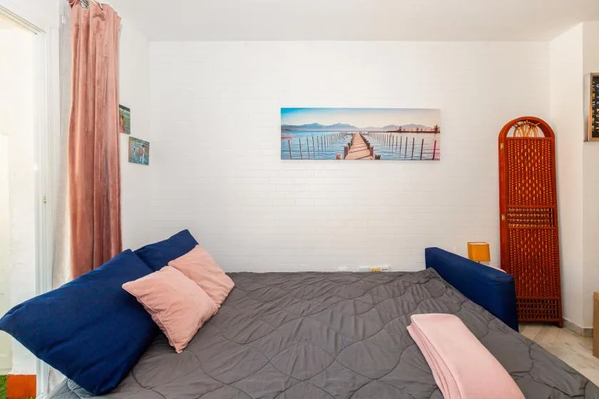 A bedroom with a bed, blue cushions, and a framed waterfront picture.