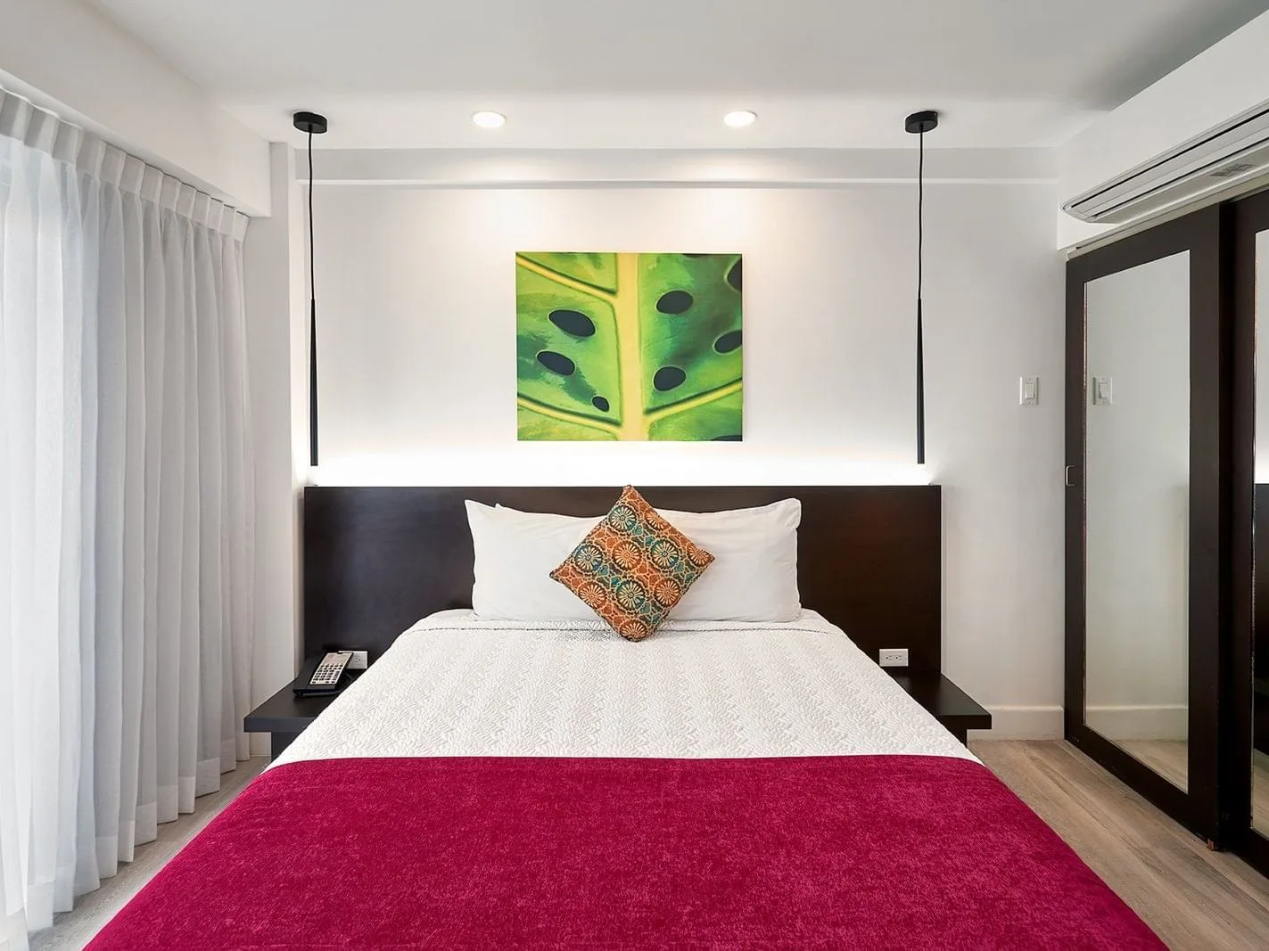 Queen bed with white linens, a red runner, and green leaf artwork in the Queen Room With Balcony.