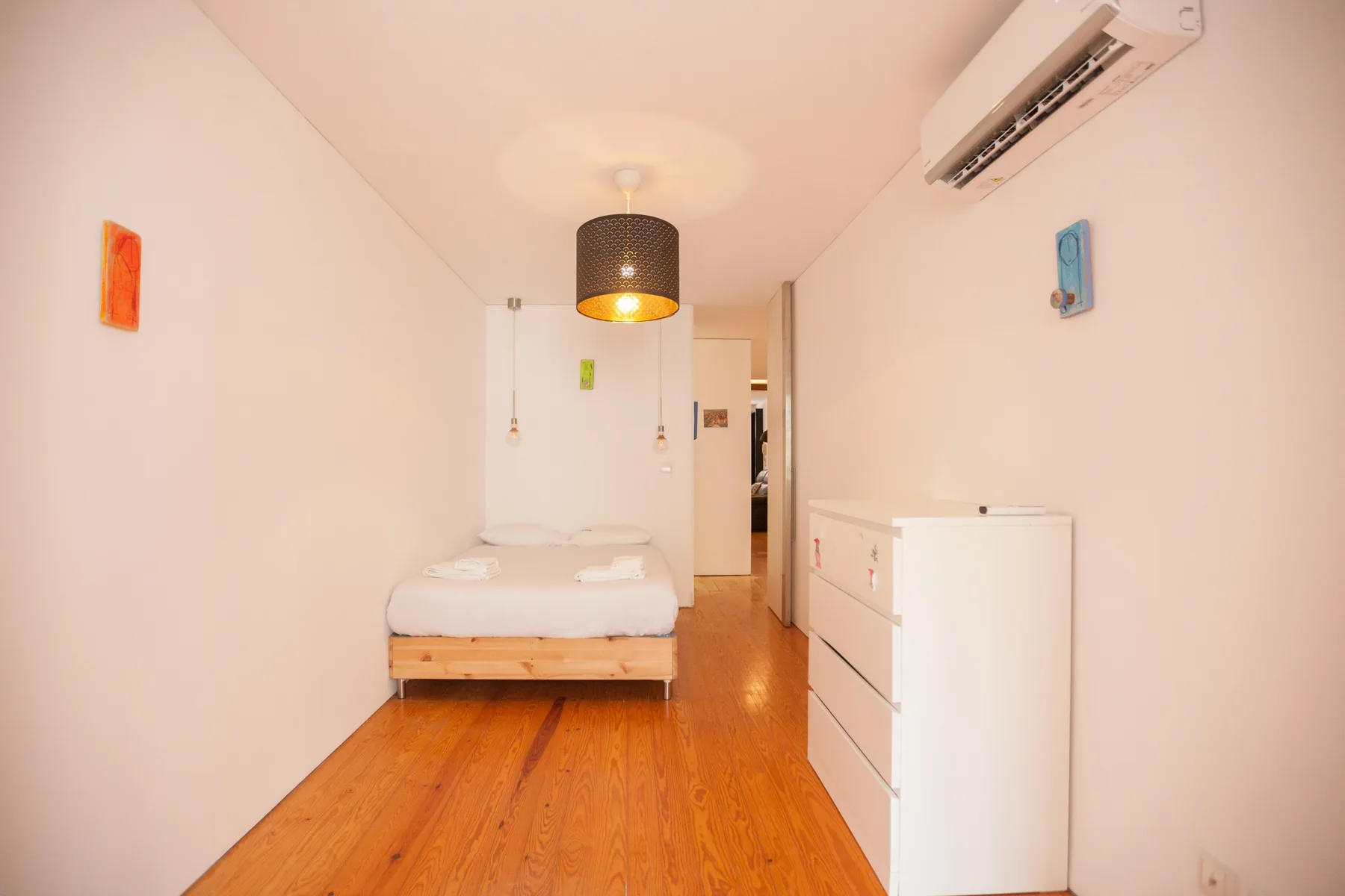A bedroom with a bed, white walls, and wooden flooring.