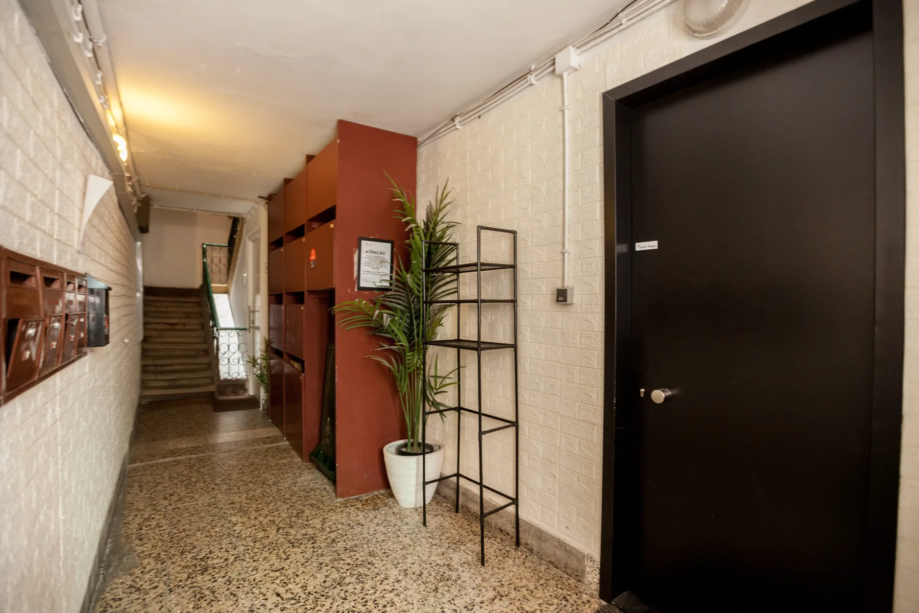 An interior hallway with a dark door, shelving, and stairs at the end.
