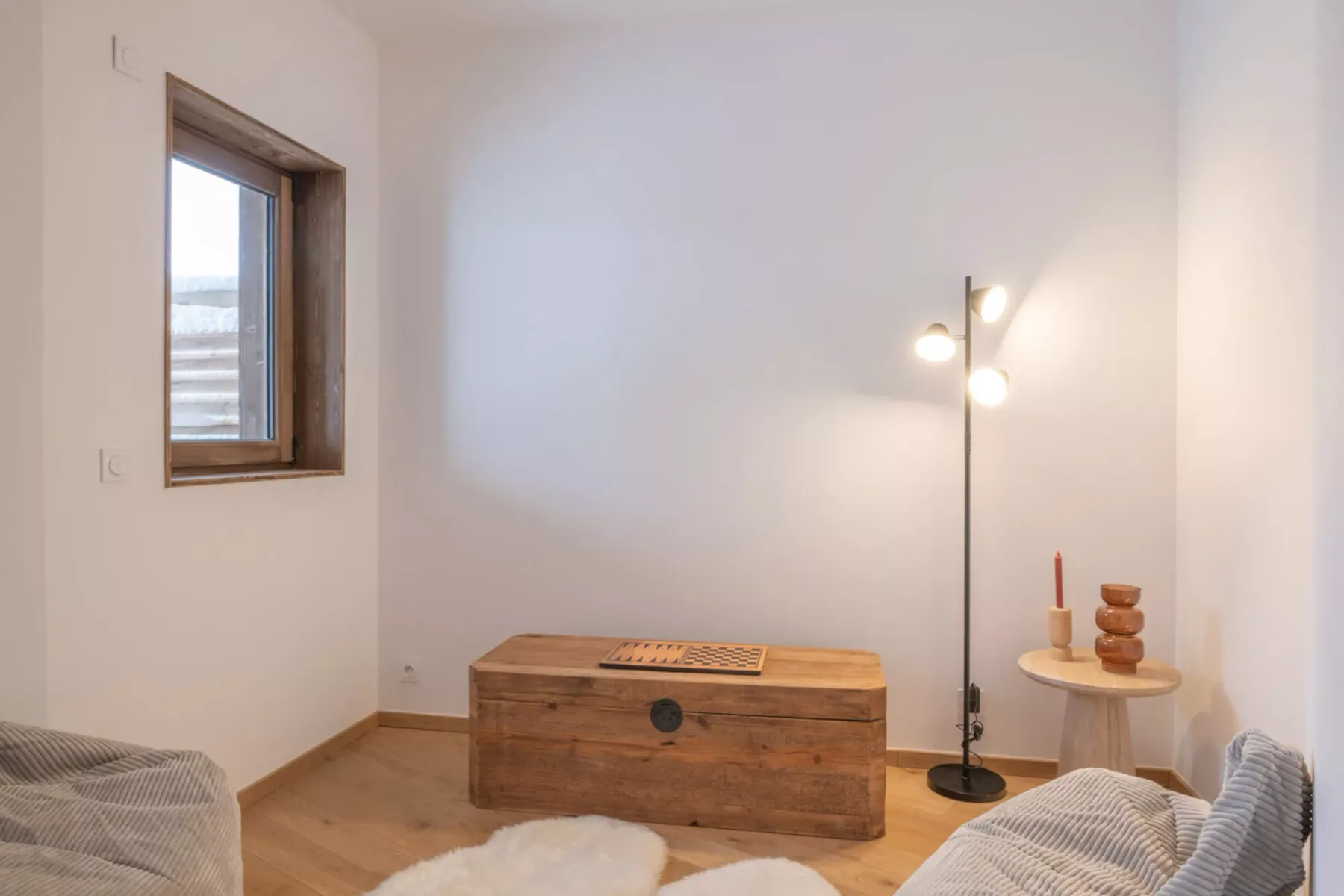 A bright sitting area with a wooden chest, floor lamp, and small side table.