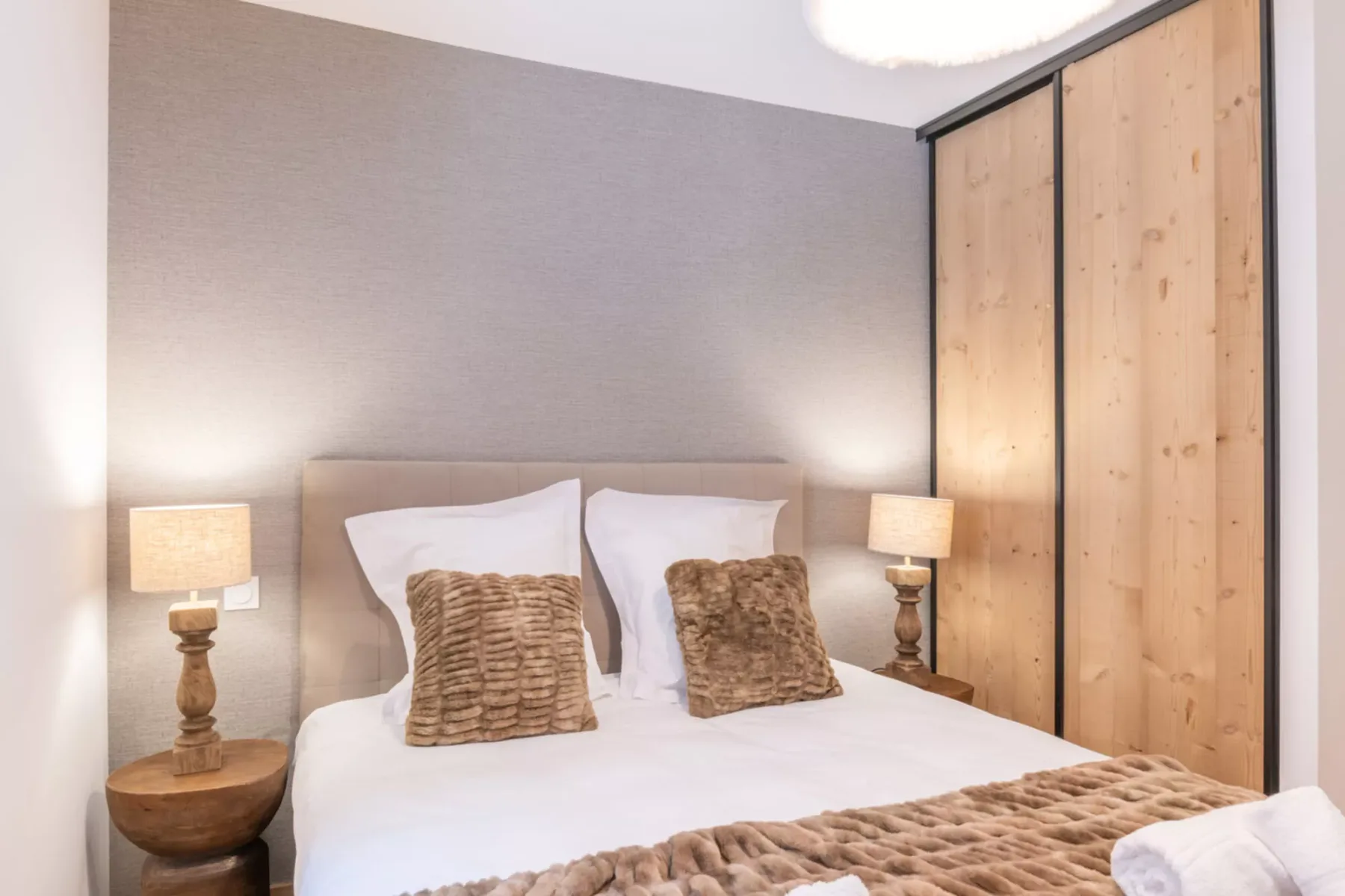 Bedroom with a bed, textured pillows, and wooden wardrobe doors.