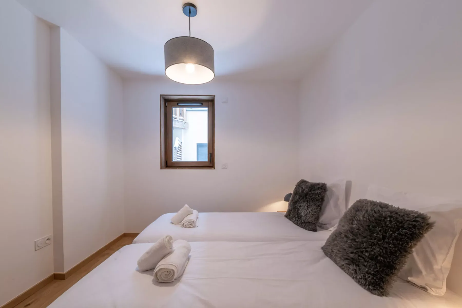 A bedroom with white bedding and a small window.