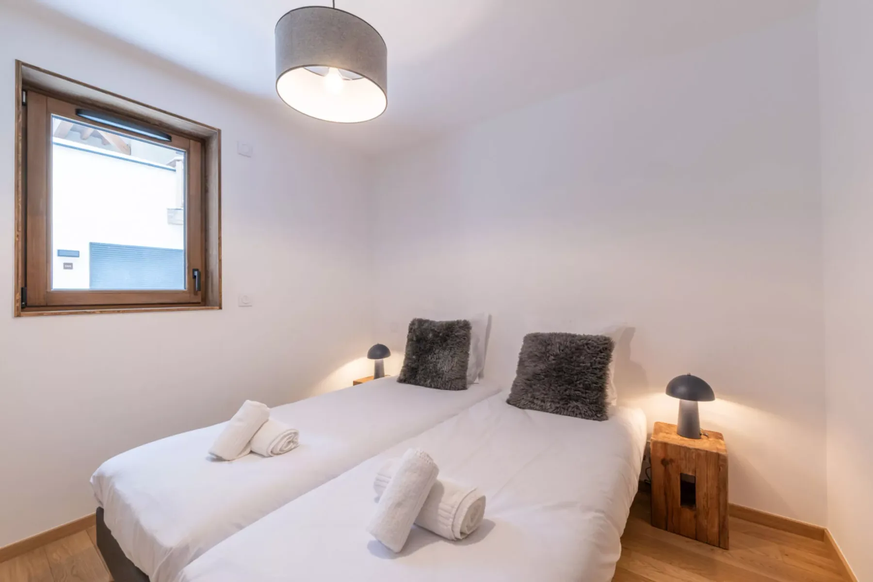 A bedroom with two beds, white bedding, and a window.
