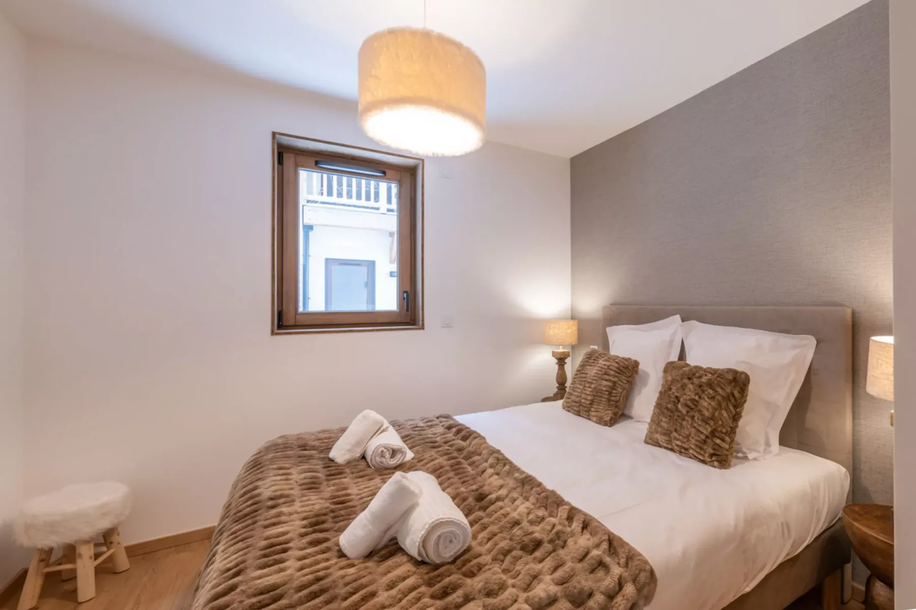 A bedroom with a double bed dressed in white linens and brown cushions.