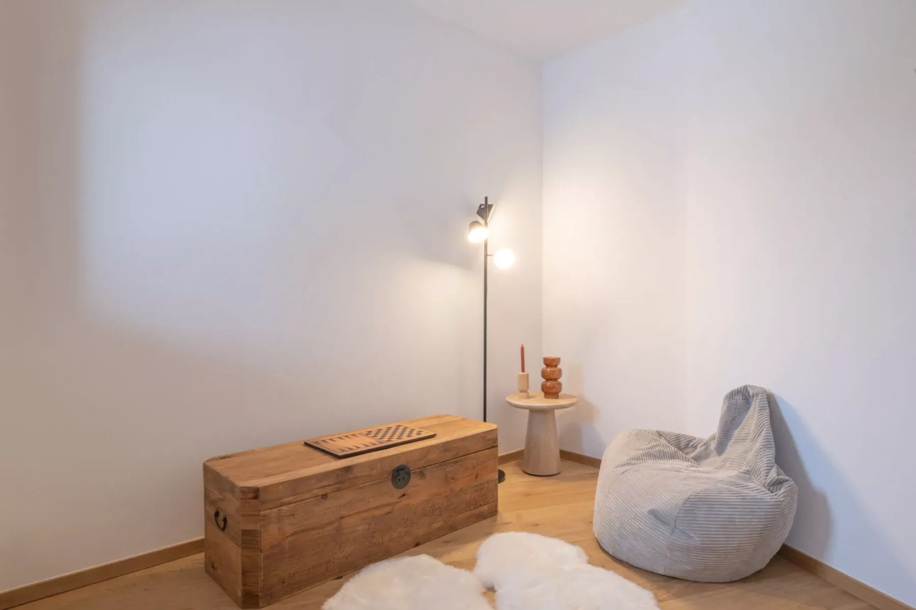 A simple sitting area with a wooden chest, floor lamp, and beanbag chair.