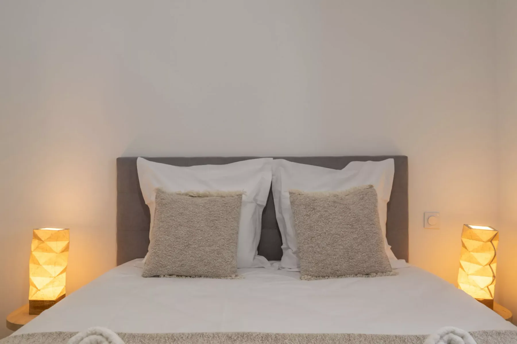 A neatly made bed with pillows and warm bedside lighting.