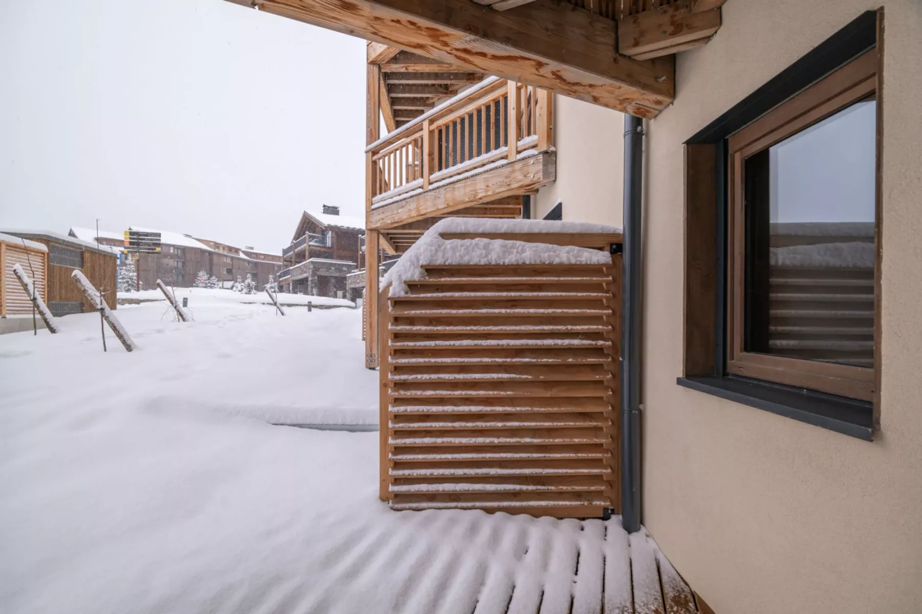 Snow covers the outdoor walkway beside wooden balconies and a window.