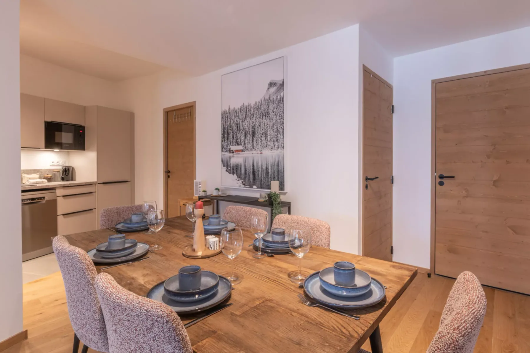 A dining area with a wooden table set with dishes beside a compact kitchen.