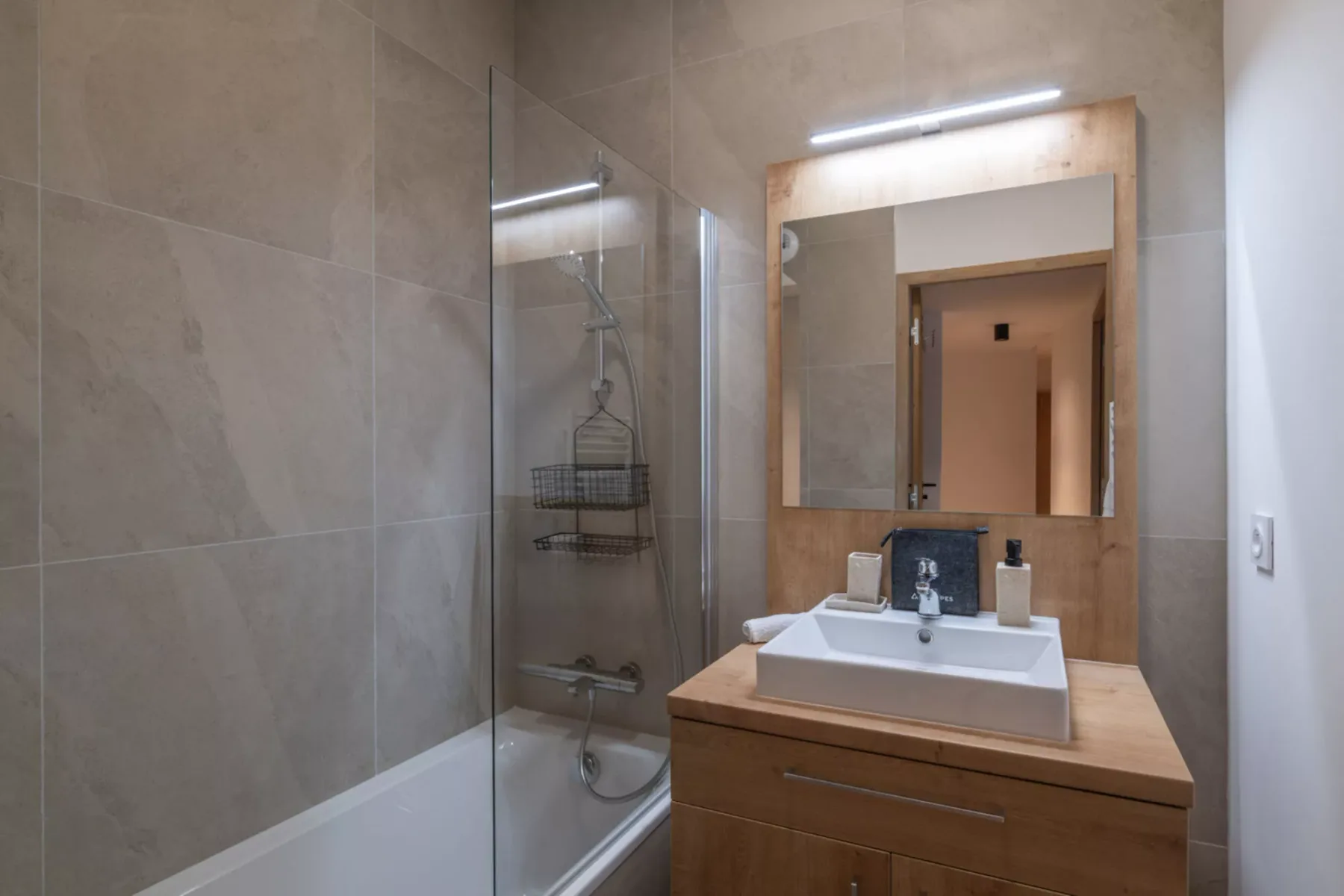 A tiled bathroom with a glass shower, sink, and mirror.