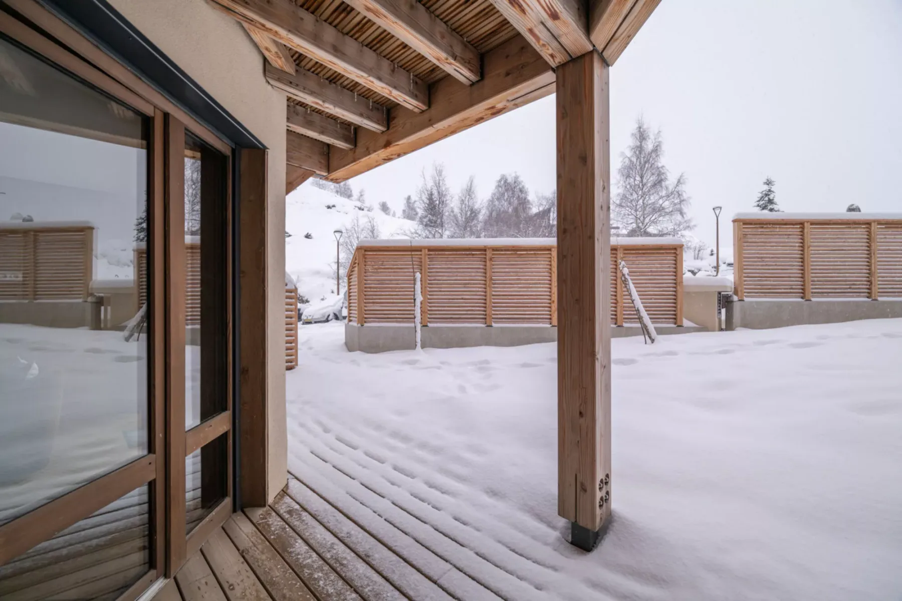 A covered wooden deck overlooks a snow-covered outdoor area with slatted screens.