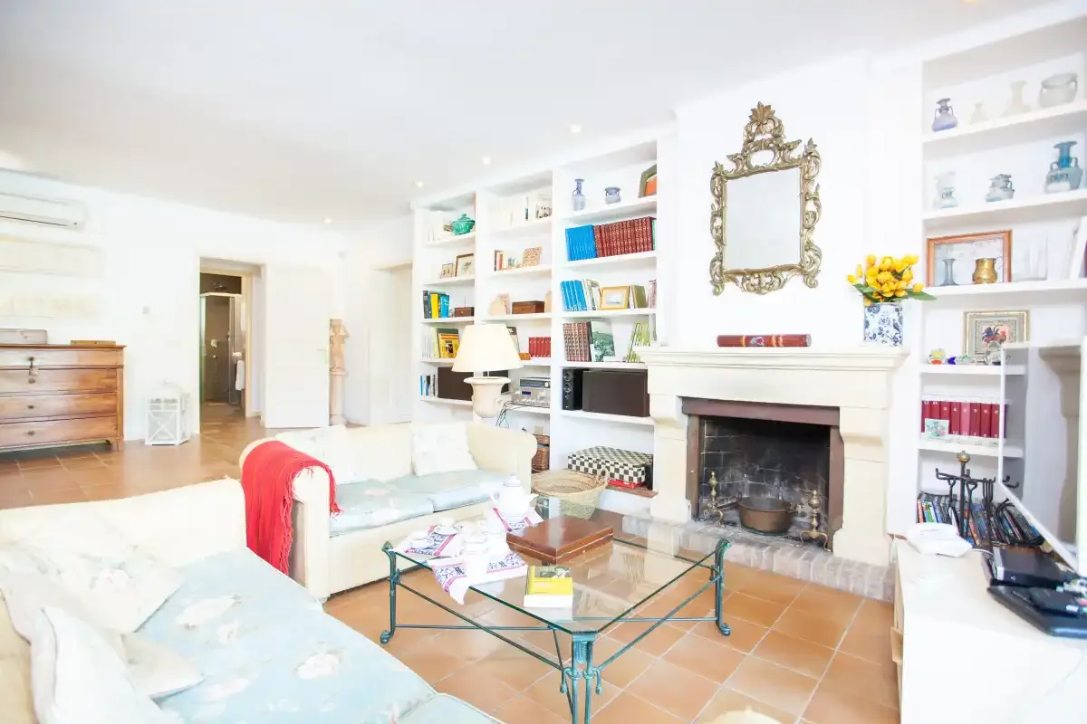 A bright living room with pale seating, a glass coffee table, and a fireplace.