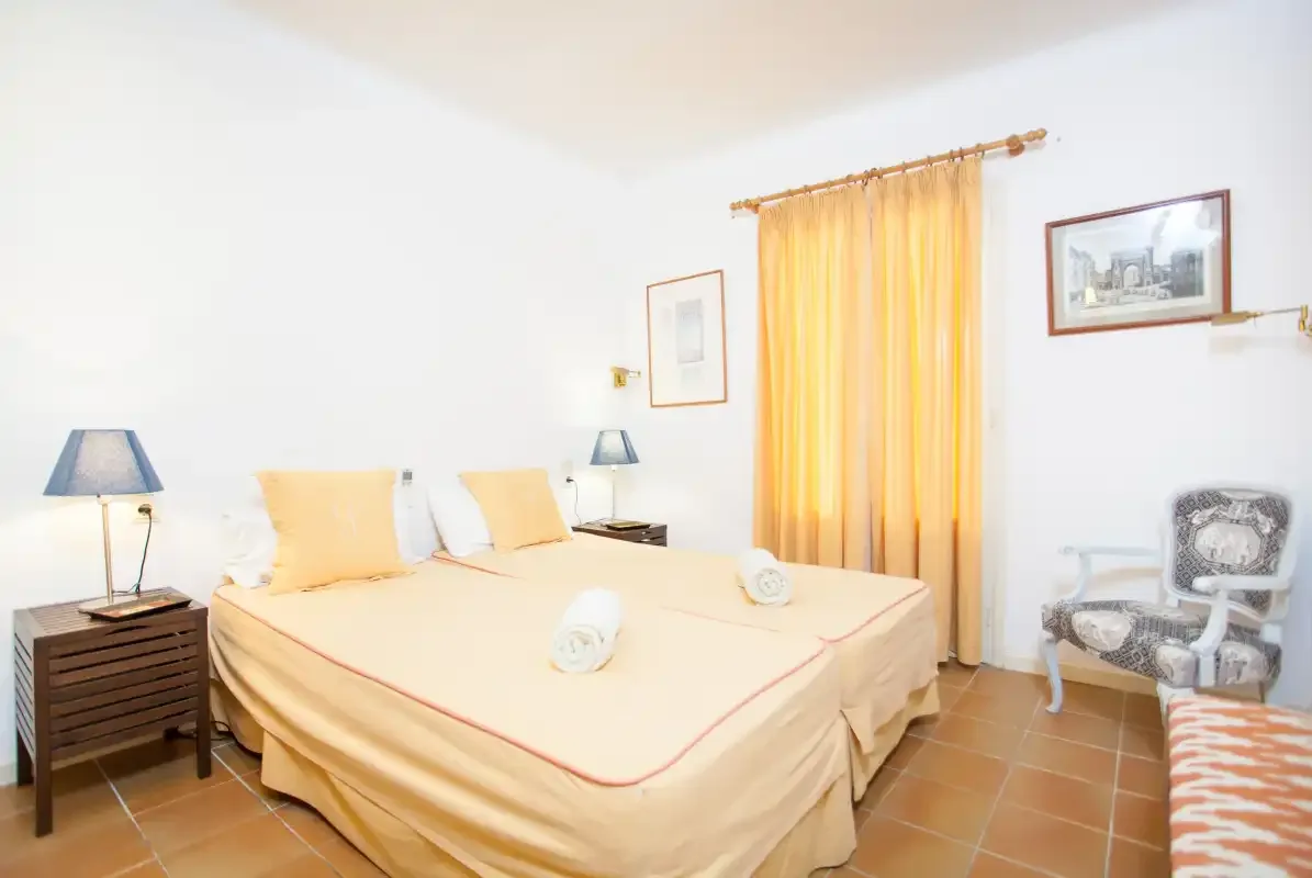 A bedroom with a double bed, bedside tables, and a sunlit window.
