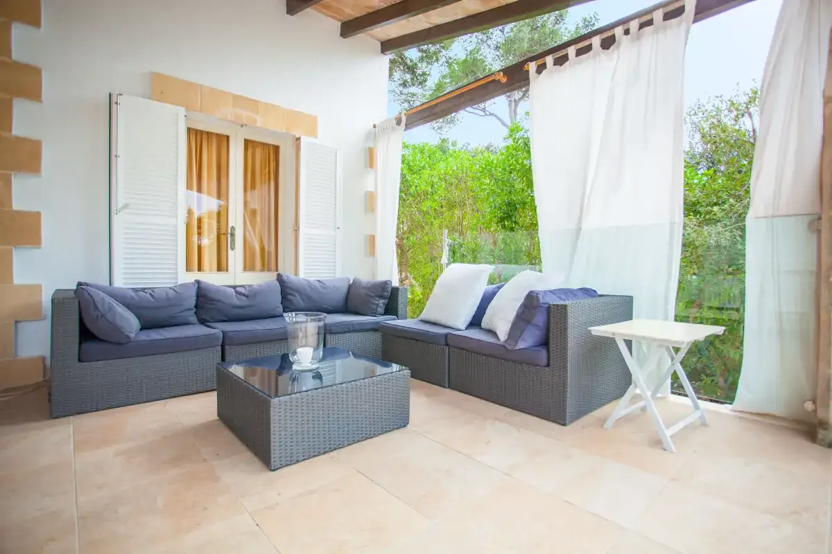 A covered patio seating area with wicker furniture and sheer curtains.