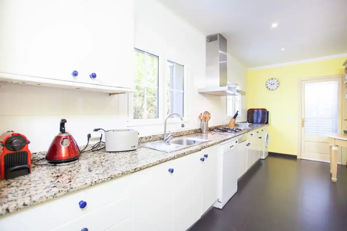 A bright kitchen with a long countertop, sink, and cooking appliances.