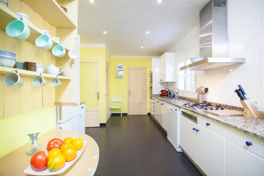 A bright kitchen with white cabinets, a long countertop, and open shelving.