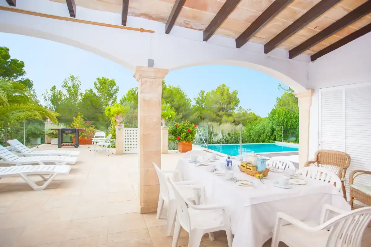 A covered outdoor dining area overlooks a swimming pool and garden.