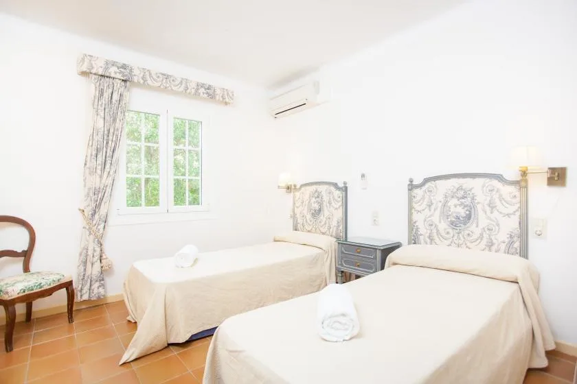 A bright bedroom with two beds, a window, and patterned curtains.