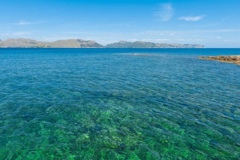A clear blue sea stretches toward a distant mountainous coastline.