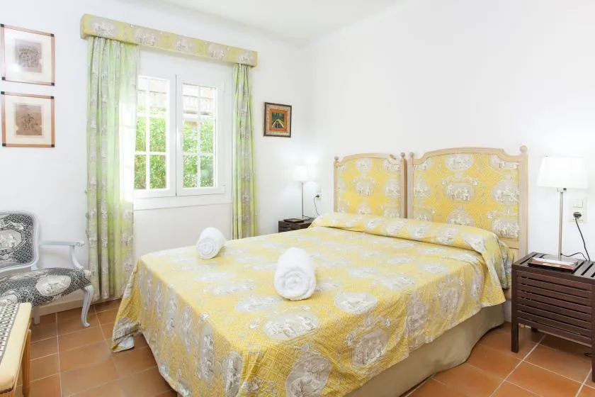 A bedroom with a yellow patterned bedspread, a window, and green curtains.