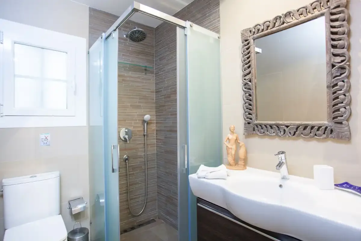 A bathroom with a glass shower, toilet, and sink beneath a wall mirror.
